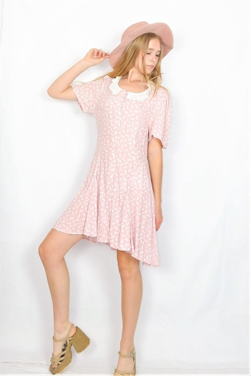 Photo shows full length photo of model wearing a baby pink bowtie polka dot printed mini shift dress with a lace collar.