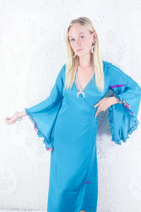 Model shows front view of our Venus maxi wrap dress. Wrap dress design with floaty bell sleeves. By All About Audrey.