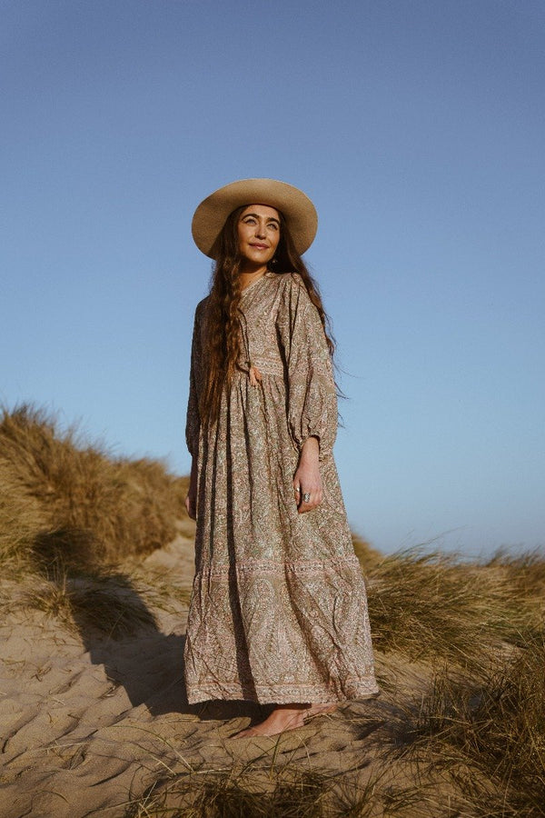 photograph of model on beach wearing bohemian style florence maxi dress with drop hem and balloon sleeve in sage and pink paisley pattern by all about audrey
