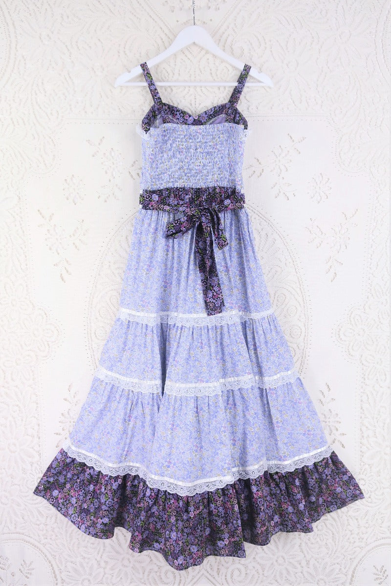 Full back product flat lay shot of the Prairie Gunne Sax inspired Darcy dress in Highland Heather. Showing a clearer view of the behind features of the dress. Including the frill tiered maxi skirt, ruched stretchy adjustable free size back and waist with additional back waist tie detailing, Main cotton fabric is a combination of two ditsy boho floral tonal lilac prints by all about audrey
