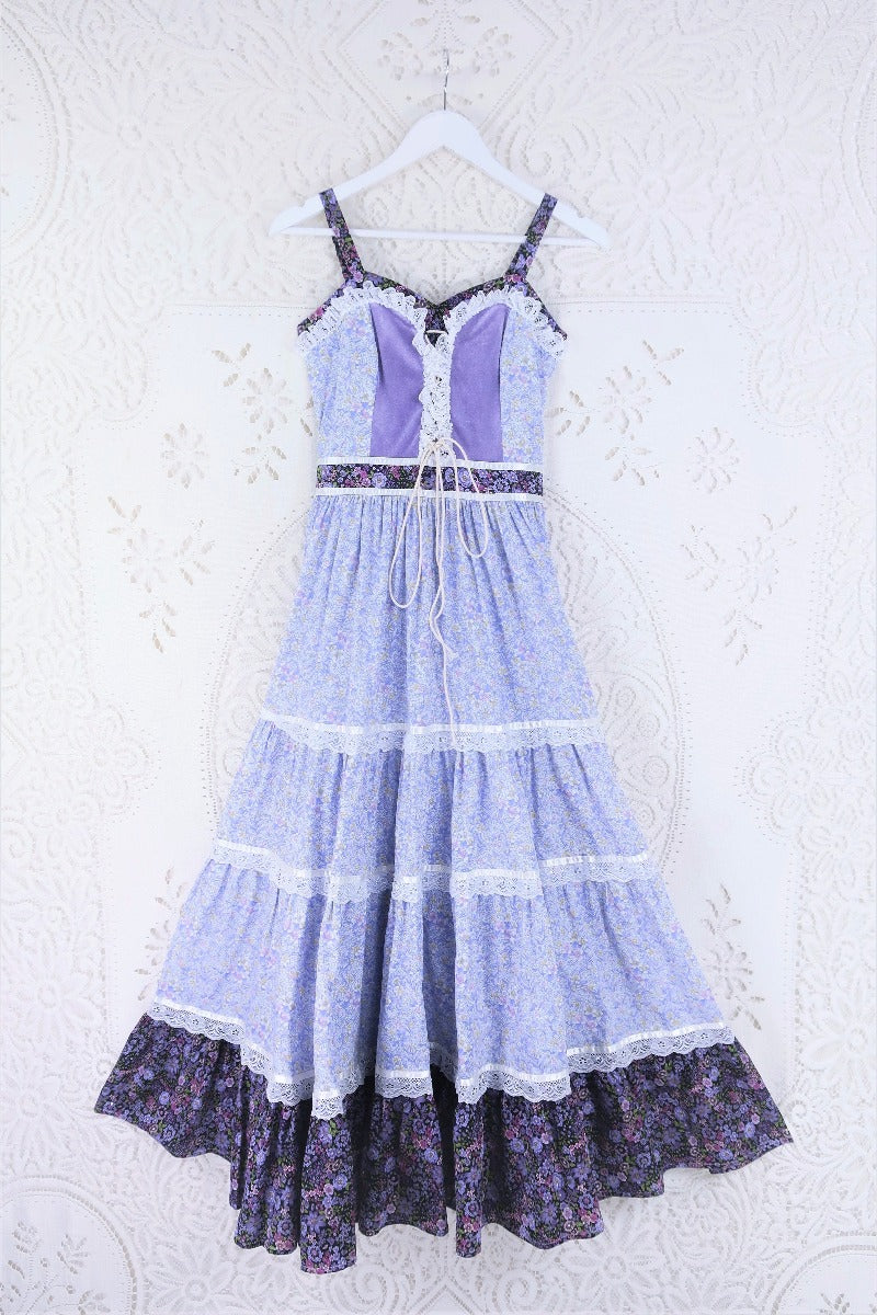 Full front product flat lay shot of the Prairie Gunne Sax inspired Darcy dress in Highland Heather. Showing a clearer view of all aspects of the dress including the frill tiered maxi skirt, fitted waist and bodice with a corset tie up front, velvet and lace detailing. Main cotton fabric is a combination of two ditsy boho floral tonal lilac prints by all about audrey