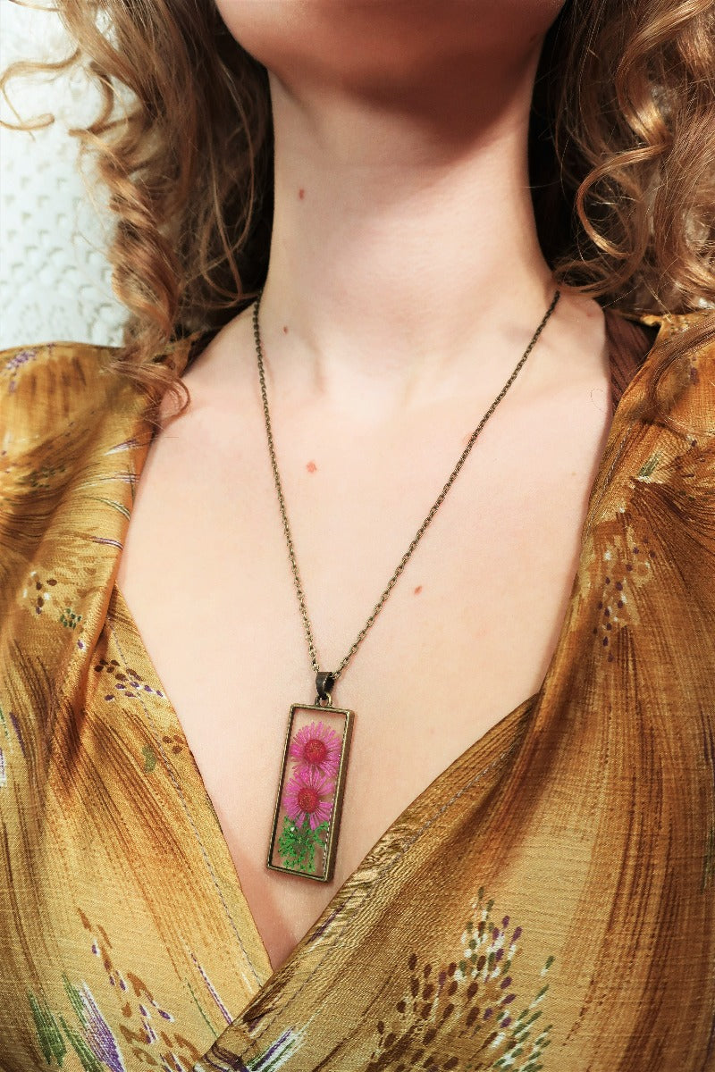 close up model wears pink dried flower pendant in brass rectangle shape on chain from our vintage inspired jewellery and gifts collection by all about audrey